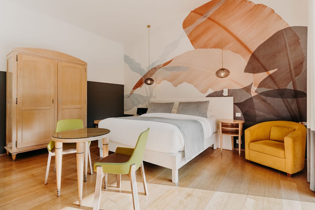 A modern bedroom with a bed, a wooden wardrobe, a round table, two chairs, and a yellow armchair.