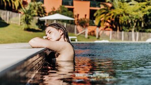 A person relaxing by a pool with a building and palm trees in the background. - Les Frères Ibarboure (Bidart)