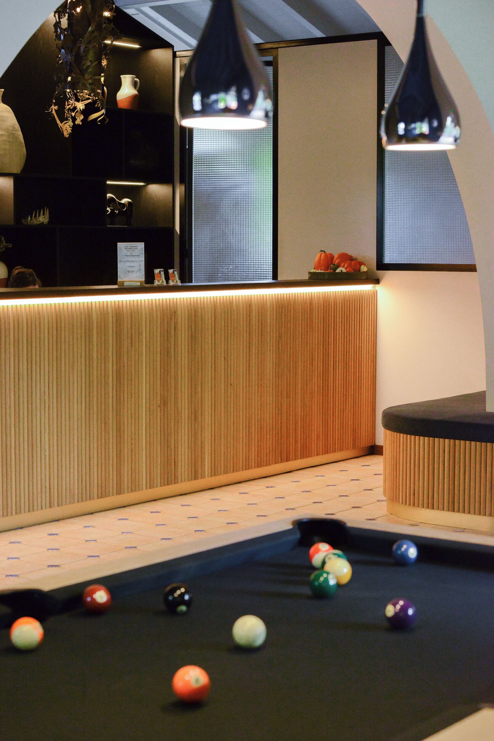 A pool table with balls, a wooden reception desk, and pendant lighting.