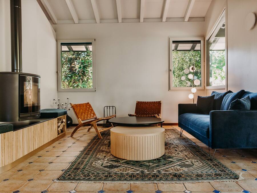 Una sala moderna con chimenea, una mesa de centro redonda de madera, un sofá azul y una alfombra estampada.