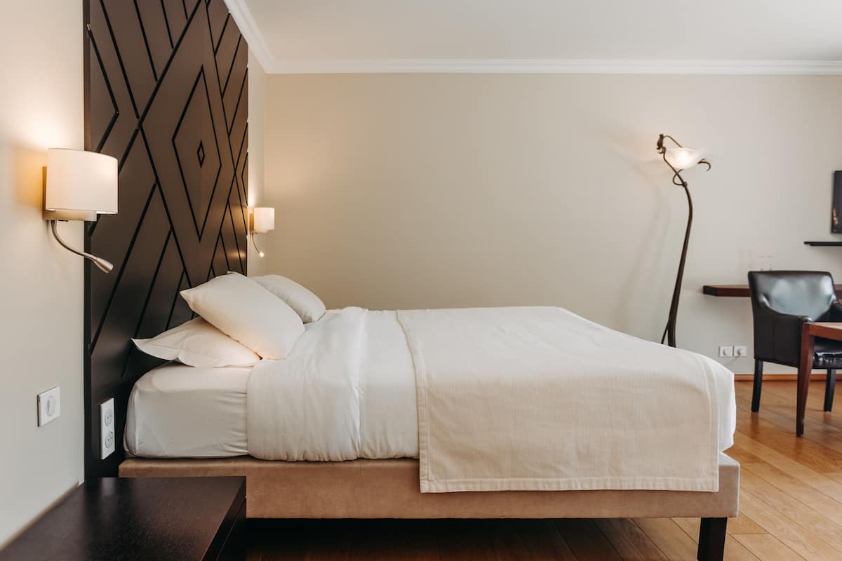 A neatly made bed with a headboard, bedside lamps, and a desk with a chair.