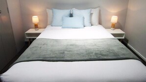 A neatly made bed with a grey blanket, two bedside lamps, and a series of pillows. - Pohutu Lodge Motel (Rotorua)