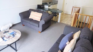 A compact living space with a sofa, a coffee table, a dining table, and a kitchen area. - Pohutu Lodge Motel (Rotorua)