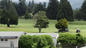 A golf course with a clubhouse, trees, and a mountainous backdrop. - Pohutu Lodge Motel (Rotorua)