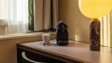 A hotel room with a wooden desk, a coffee maker, a tea set, and a lamp.