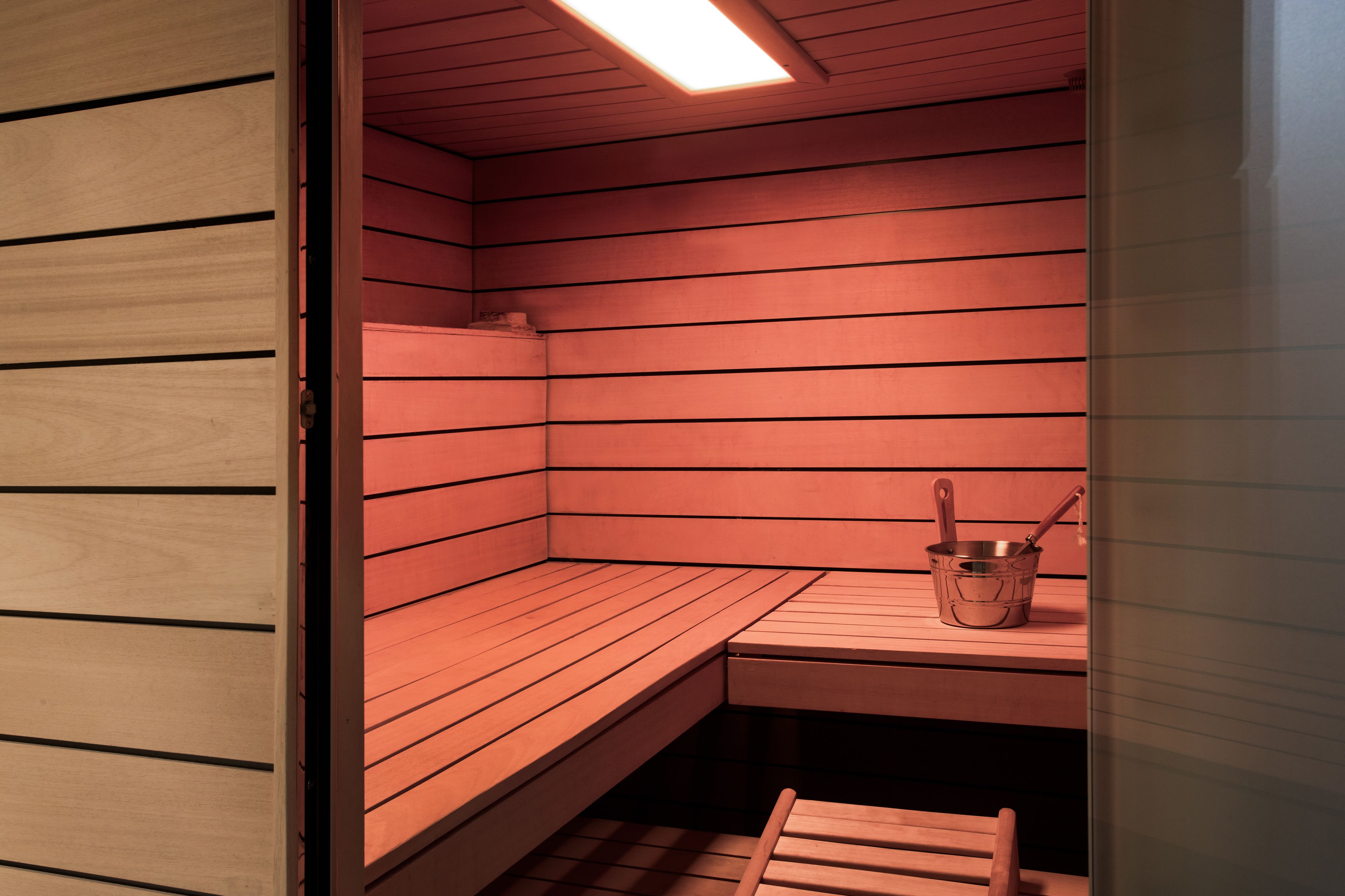 A sauna with wooden benches and a metal bucket.