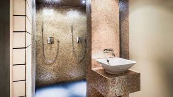 A modern bathroom with mosaic tile walls, a large sink, and two showerheads.