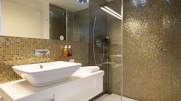 Un baño moderno con un lavamanos grande de color blanco, un box de ducha de vidrio y paredes con mosaicos.