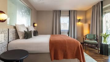 A modern hotel room with a large bed, a small table, a chair, and a potted plant.