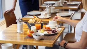 Eixordio amb taula per a dues persones, plats amb torrades, fruita i un bol de cereals.