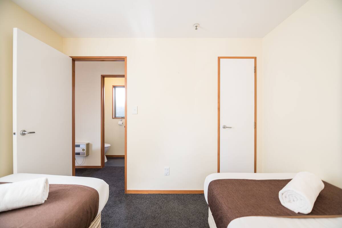 A hotel room with two beds, a bathroom, and a hallway leading to another room.