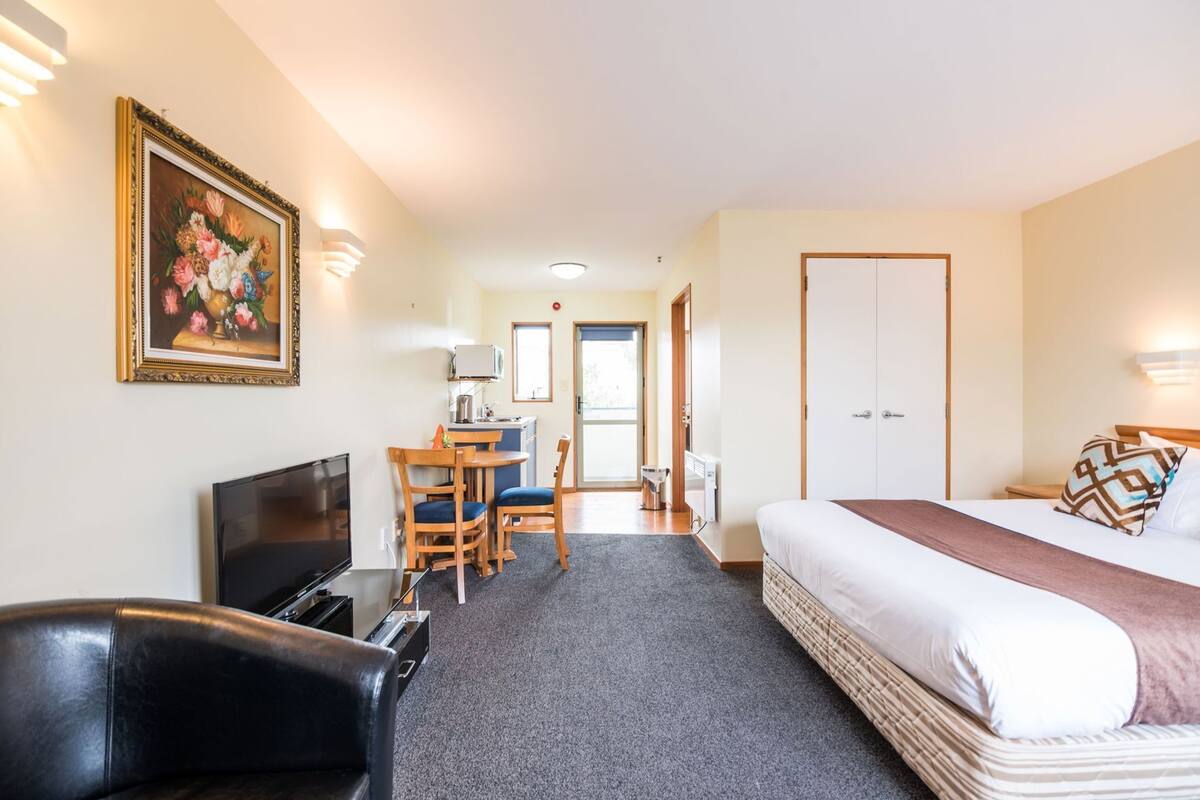 A hotel room with a bed, a desk with a chair, a television, and a painting on the wall.
