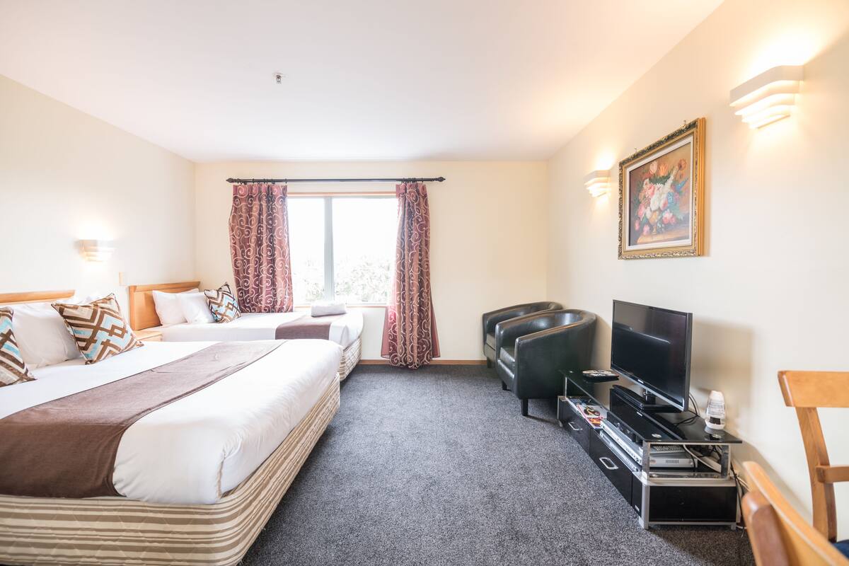 A hotel room with a bed, a TV, a seating area, and a window with curtains.