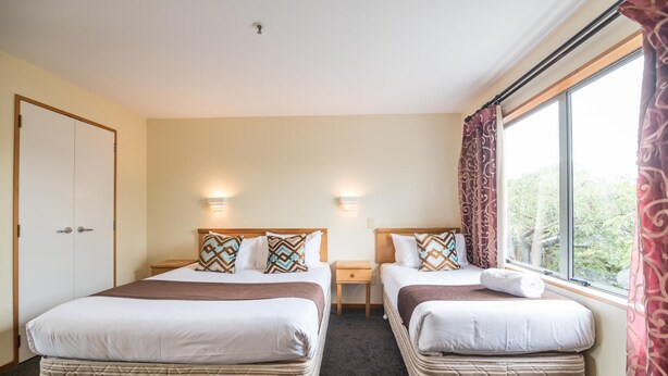 Hotelkamer met twee bedden, een garderobe, een nachtkastje en een raam met gordijnen.
