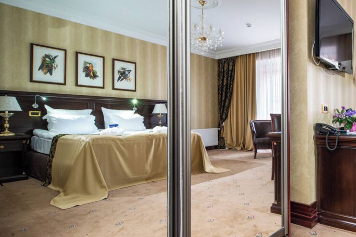 A hotel room with a bed, bedside tables, a desk with a lamp, a chair, and a television.