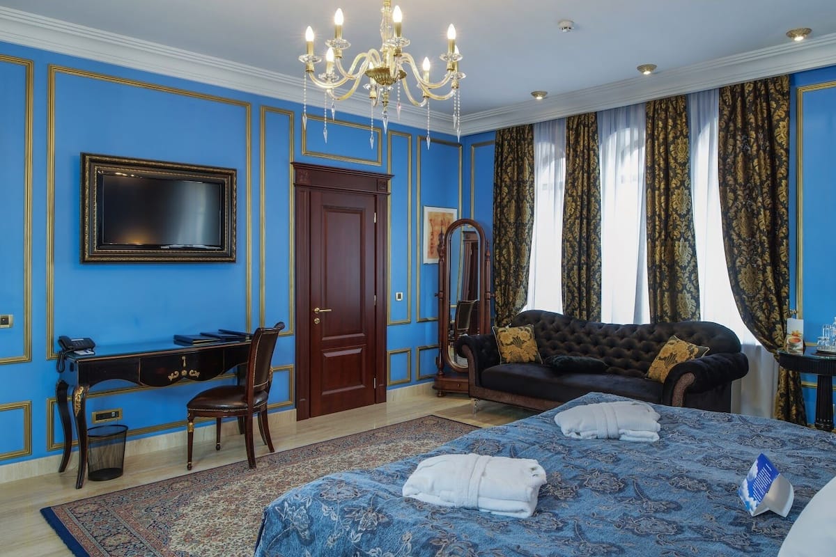 A bedroom with a large bed, a desk, a chair, a wardrobe, and a chandelier.