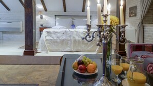 Quarto com cama, mesa de cabeceira com frutas e bebidas, e candelabro com velas.