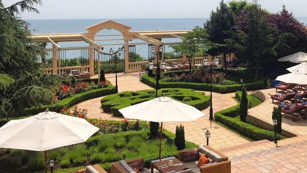 Um pátio com jardim, mobiliário de exterior, pérgola e vista para o mar.