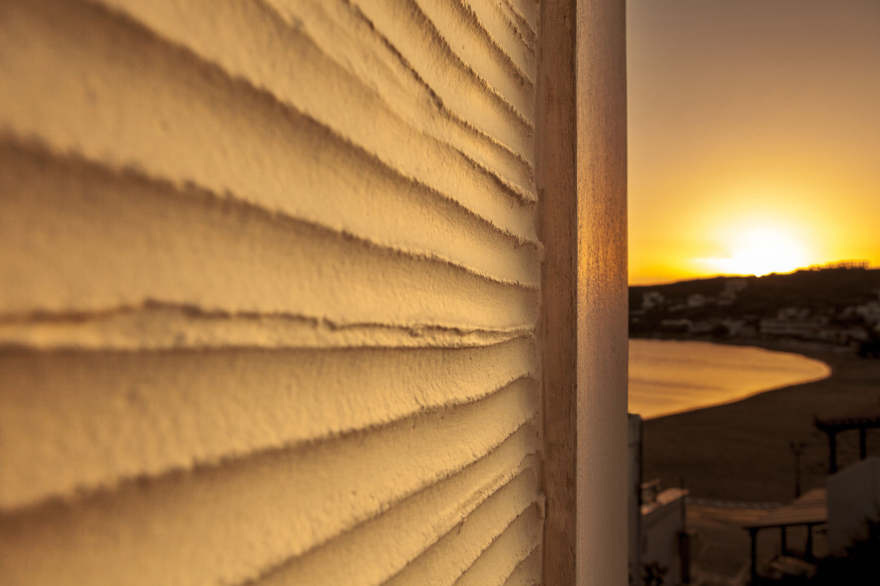 A close-up of a textured wall with a view of a sunset over a landscape.