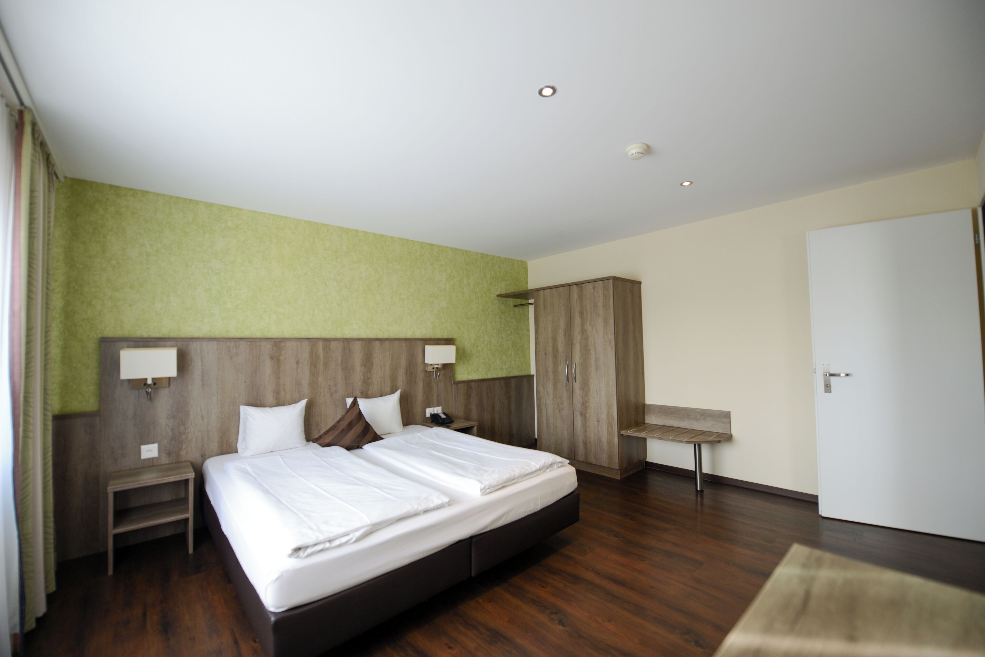 Una habitación de hotel con una cama grande, cabecero de madera, un escritorio y un armario.