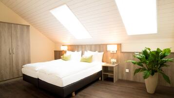 A bedroom with a large bed, wooden headboard, bedside lamps, a nightstand, and a potted plant.