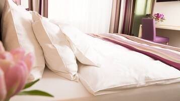 A neatly made bed with white linens, a purple chair, and a small table with a vase of flowers.