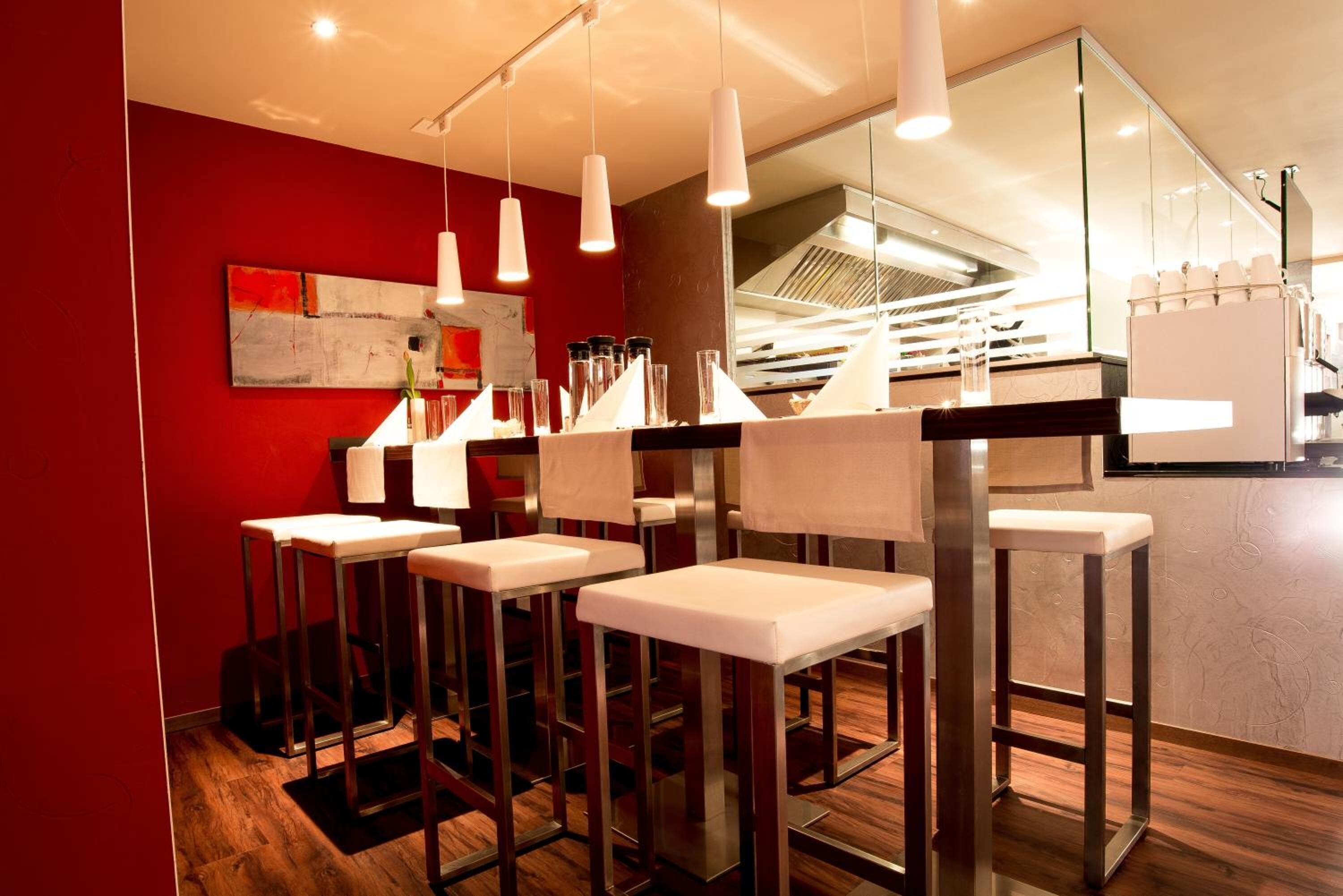 A modern bar area with high stools, pendant lighting, and a red accent wall.