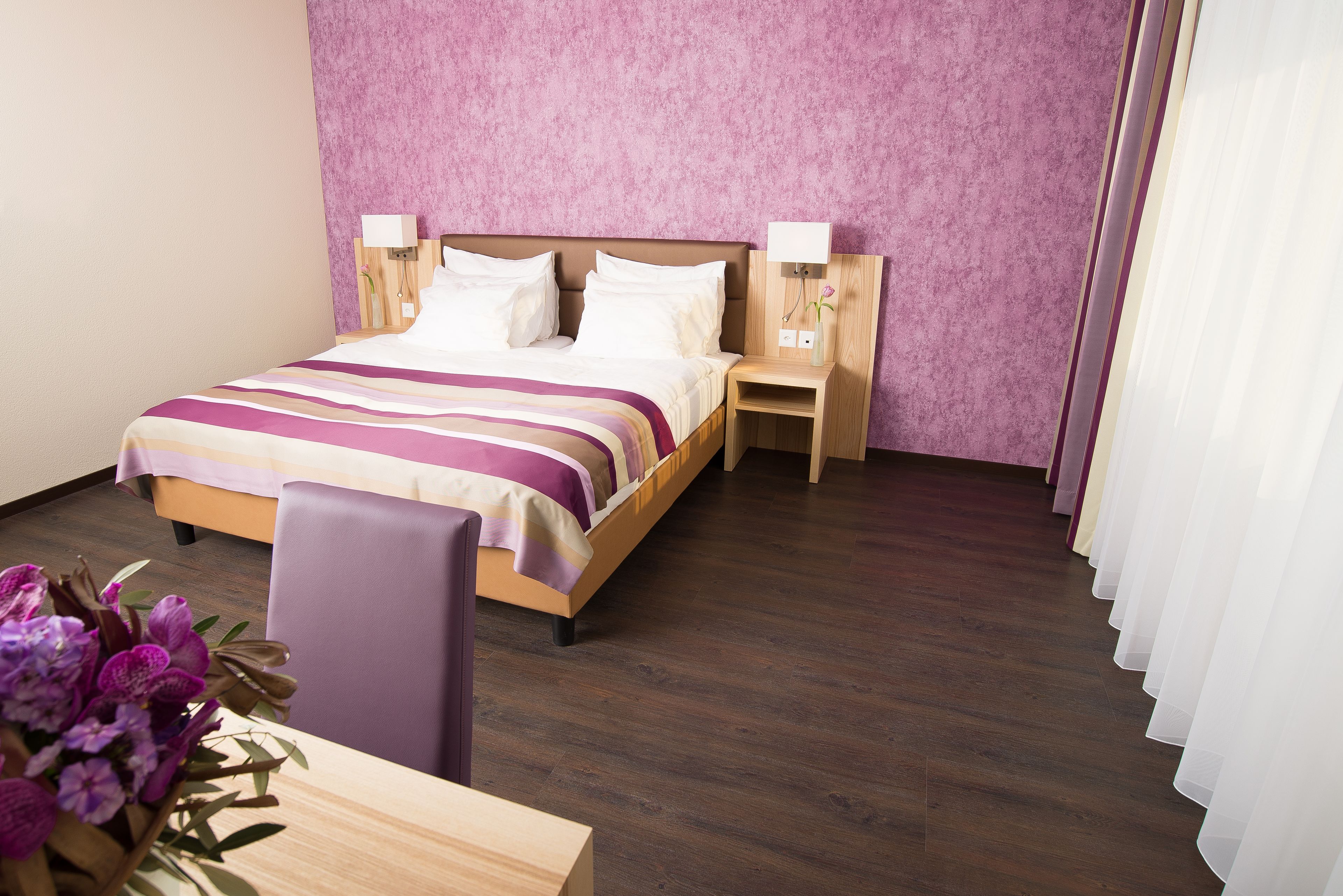 Una camera d'albergo ordinata con un letto, comodini, una sedia e una scrivania.