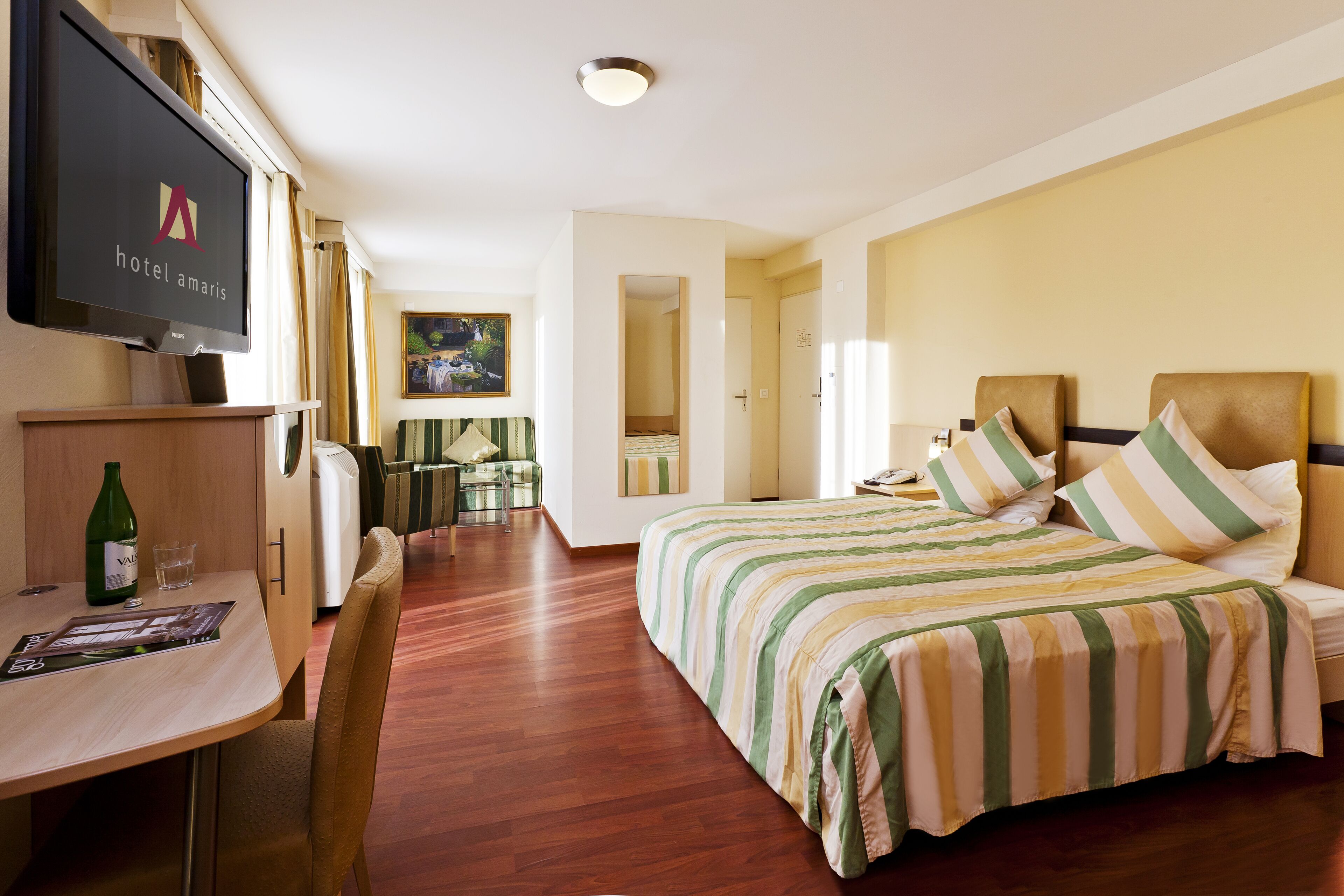 A hotel room with a bed, a TV, a desk with a chair, and a dining area.