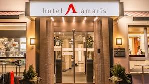 Exterior do Hotel Amaris, com entrada em destaque, plantas em vasos e uma placa.