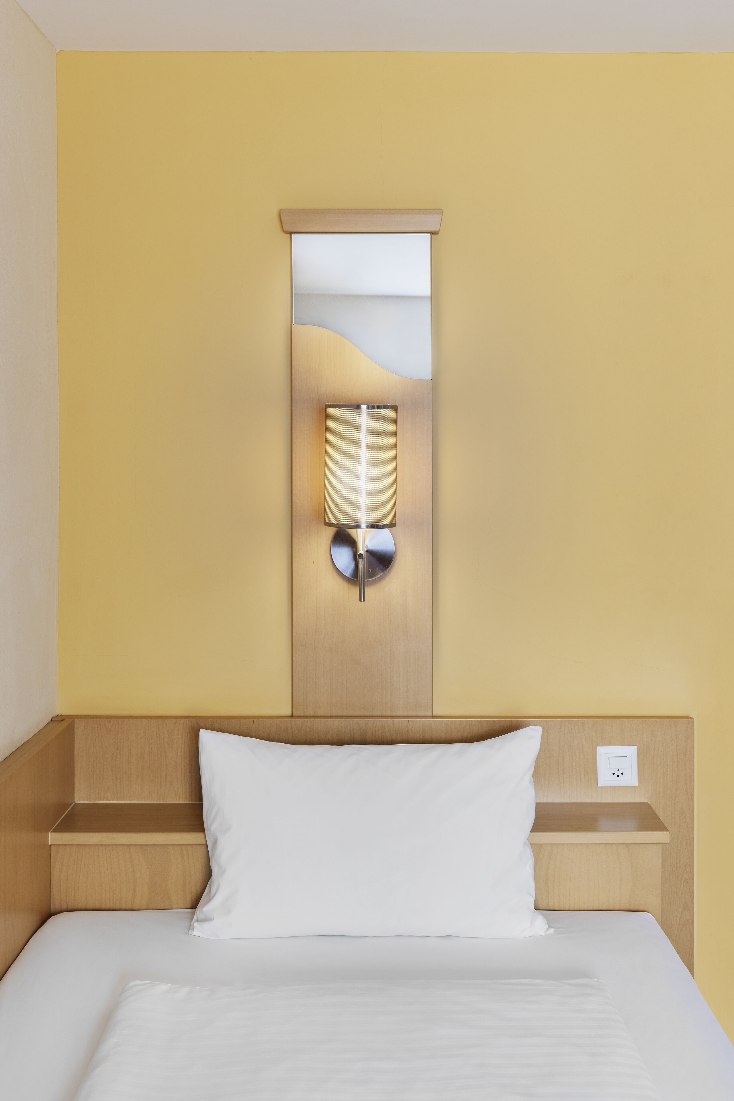 Ein Hotelzimmer mit einem Bett, einer Wandleuchte und einem Holzkopfteil.