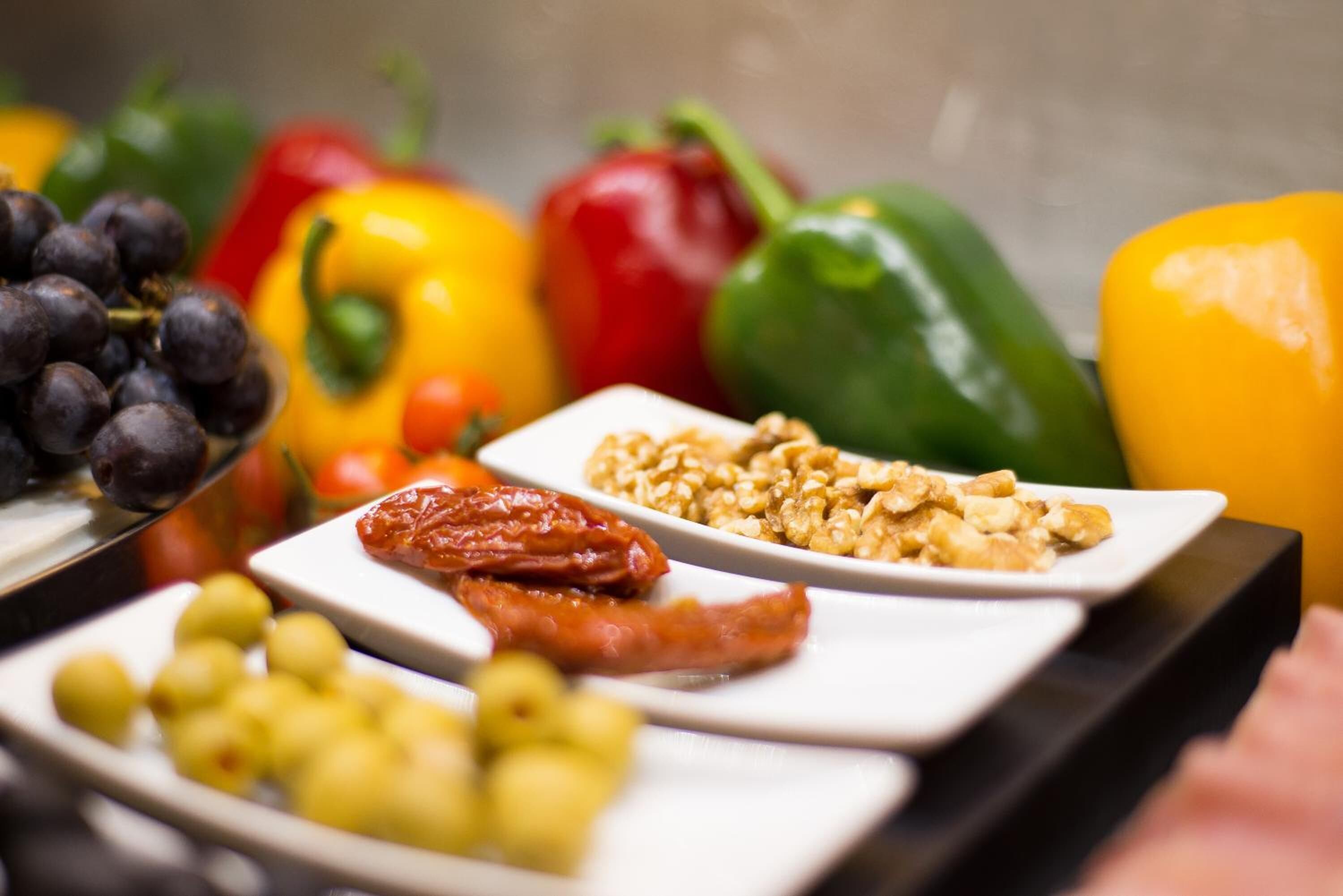 Une variété d’aliments, notamment des raisins, des noix et des olives, présentés sur des assiettes blanches.