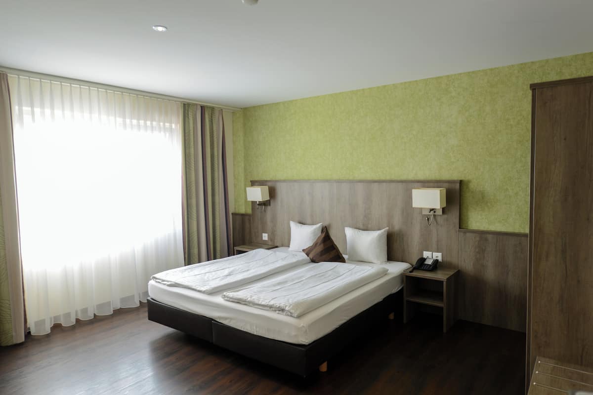 A hotel room with a large bed, two bedside tables, a nightstand, and a wardrobe.