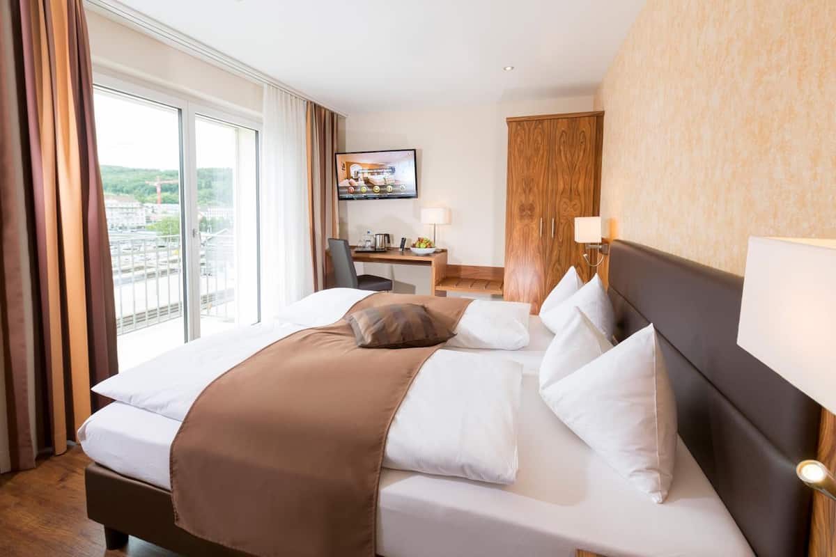 A hotel room with a large bed, a desk with a computer, a TV, and a view of the city.