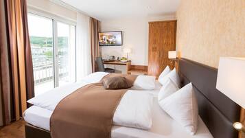 Habitación de hotel con una cama grande, un escritorio con computadora, televisor y vistas a la ciudad.