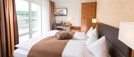 Habitación de hotel con una cama grande, un escritorio con computadora, televisor y vistas a la ciudad.