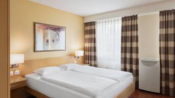 Habitación de hotel con una cama grande, dos mesitas de noche con lámparas, una obra de arte colgada en la pared, una ventana con cortinas y un calefactor portátil.