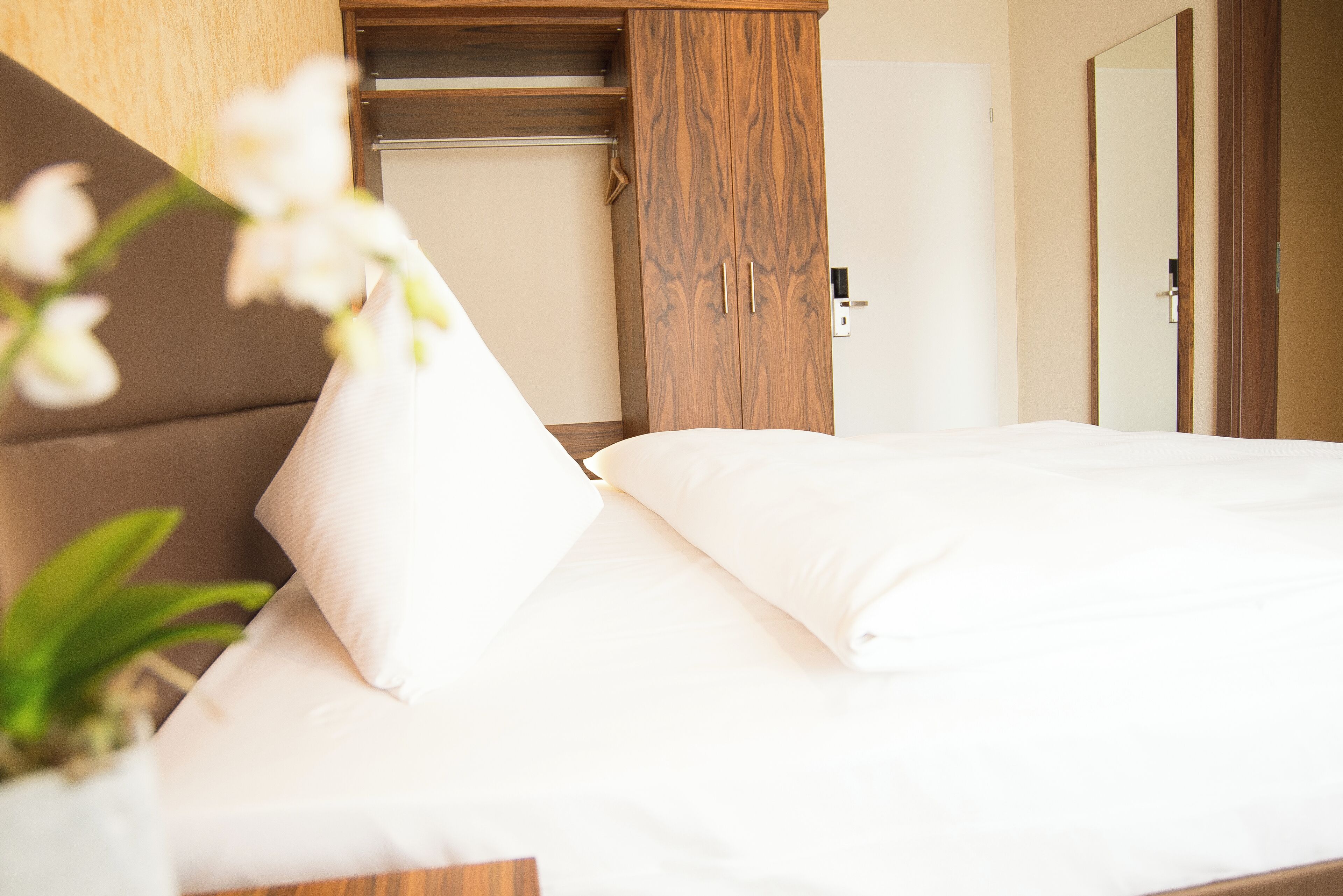 A neatly made bed with white linens, a wooden headboard, and a wooden wardrobe with two doors.