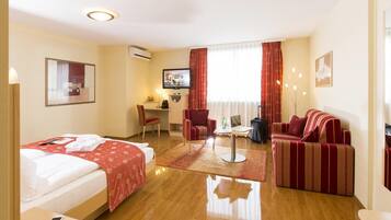 A hotel room with a bed, a sofa, a desk with a chair, a TV, and a window with curtains.