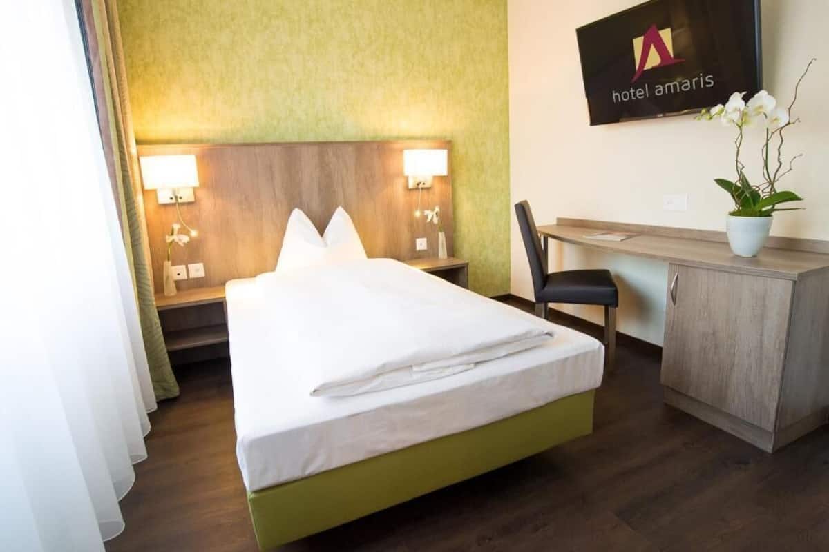 A hotel room with a bed, a desk, a chair, and a potted plant.