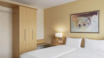 Una habitación de hotel con cama, mesita de noche, lámpara, un cuadro en la pared y armario.