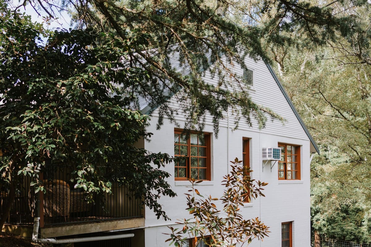 A white house with a garage, surrounded by trees and a driveway.