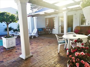 Un patio couvert avec un sol en briques, des meubles blancs et des plantes en pot.