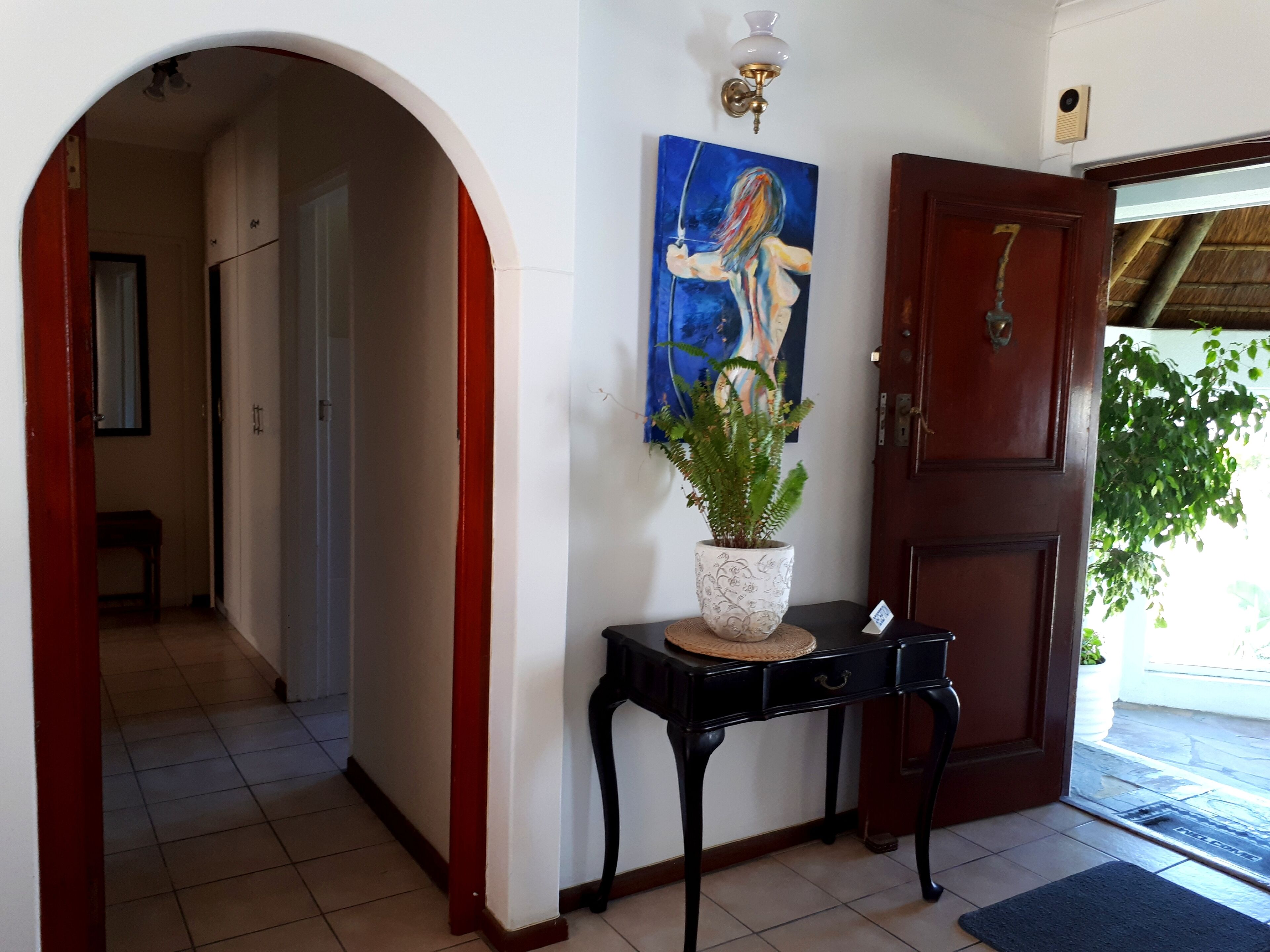 A hallway with a red door, a black table with a potted plant, and a painting on the wall.