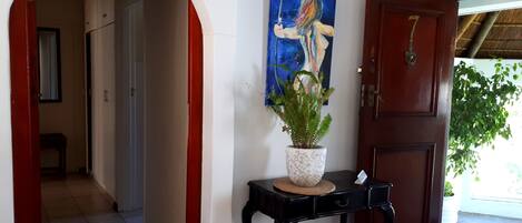 A hallway with a red door, a black table with a potted plant, and a painting on the wall.
