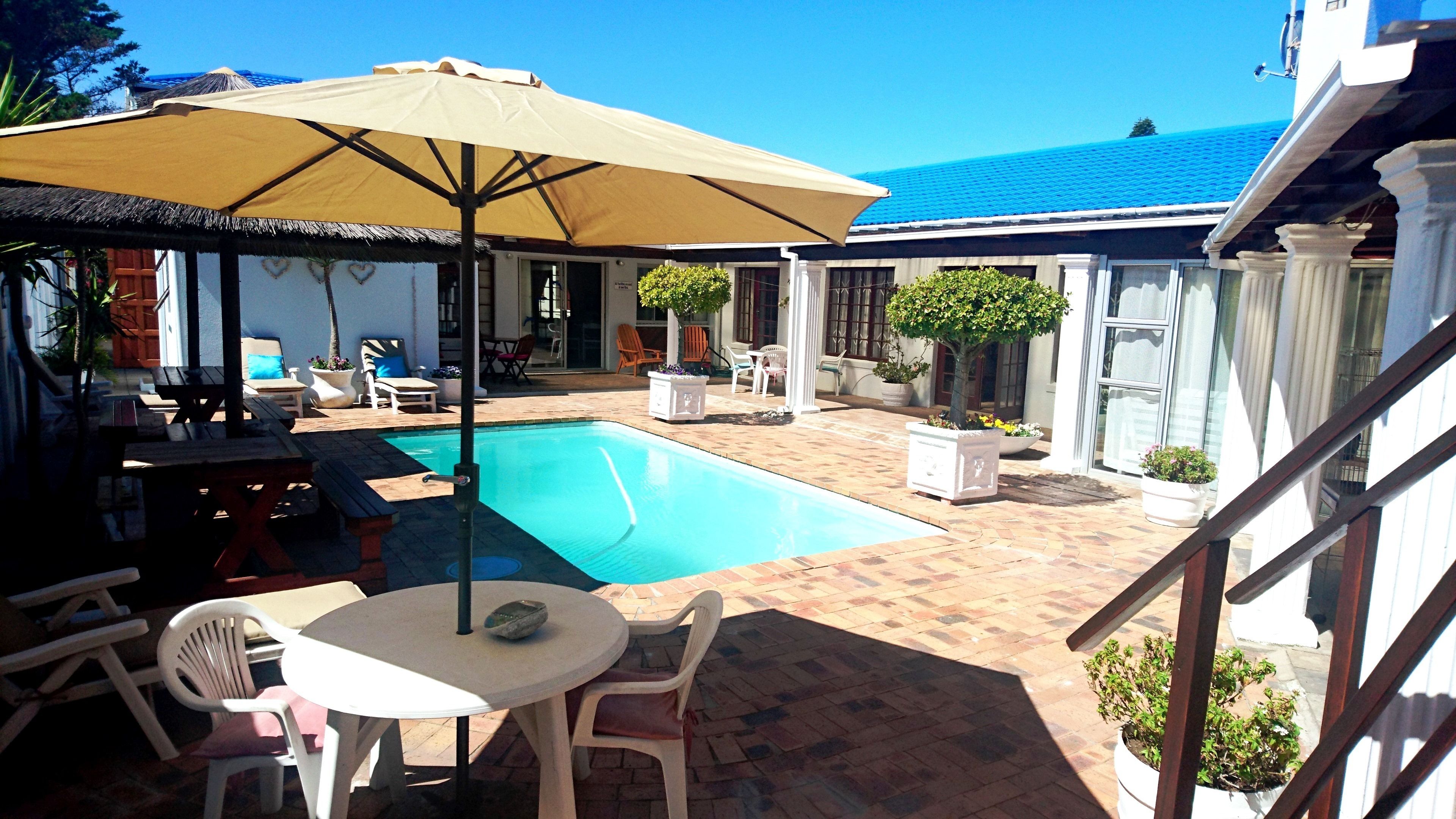A pool area with a table and chairs, a covered seating area, and potted plants.
