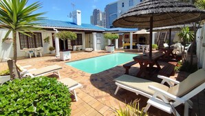 Un espace aménagé au bord de la piscine, avec des chaises longues, un parasol en chaume et une petite piscine.