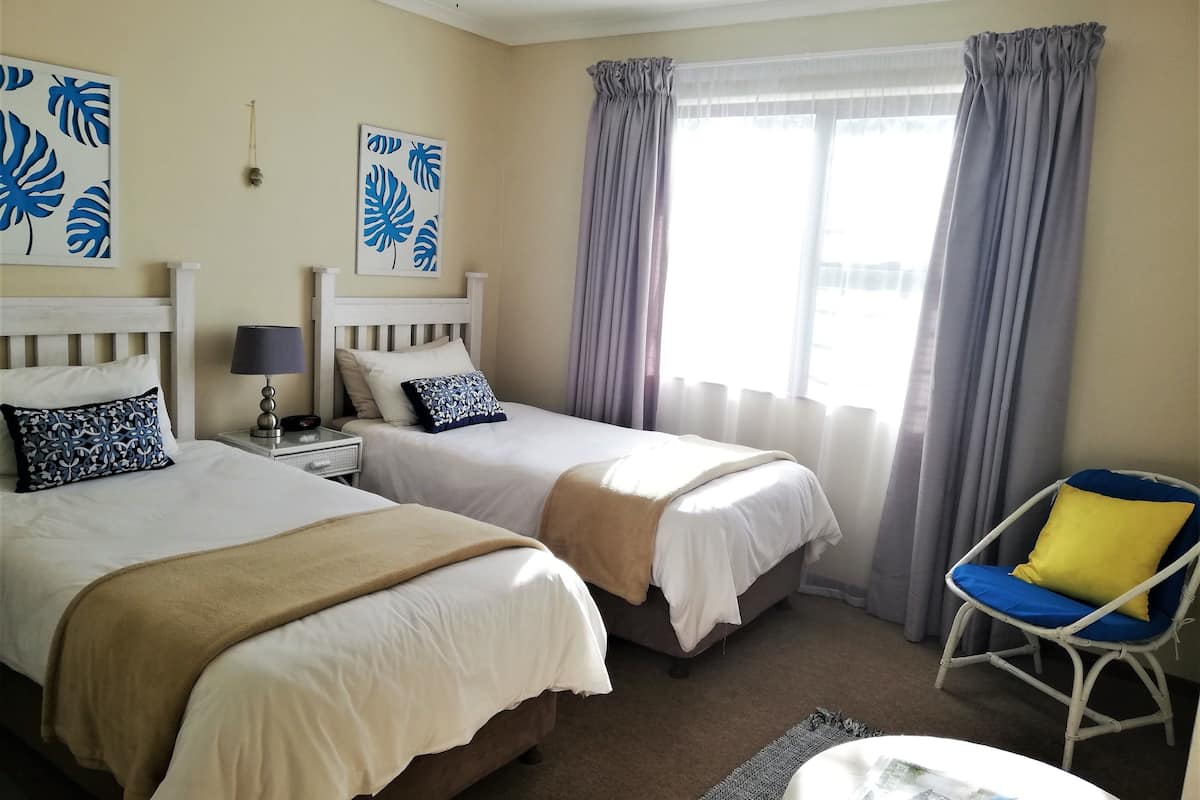 A hotel room with two beds, a chair, and a window with curtains.