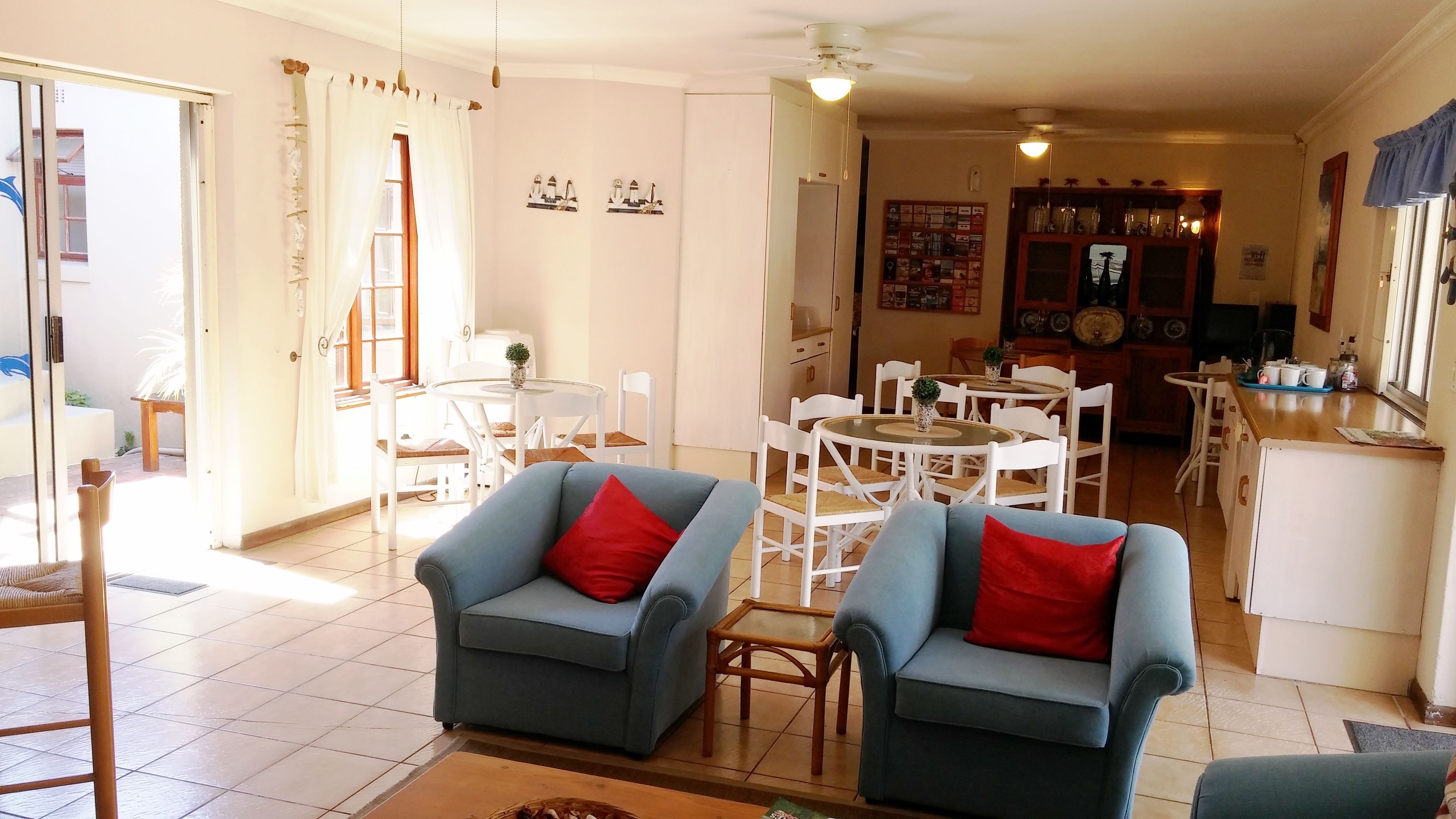 A spacious living room with two blue armchairs, a dining area with white chairs, and a kitchen visible in the background.
