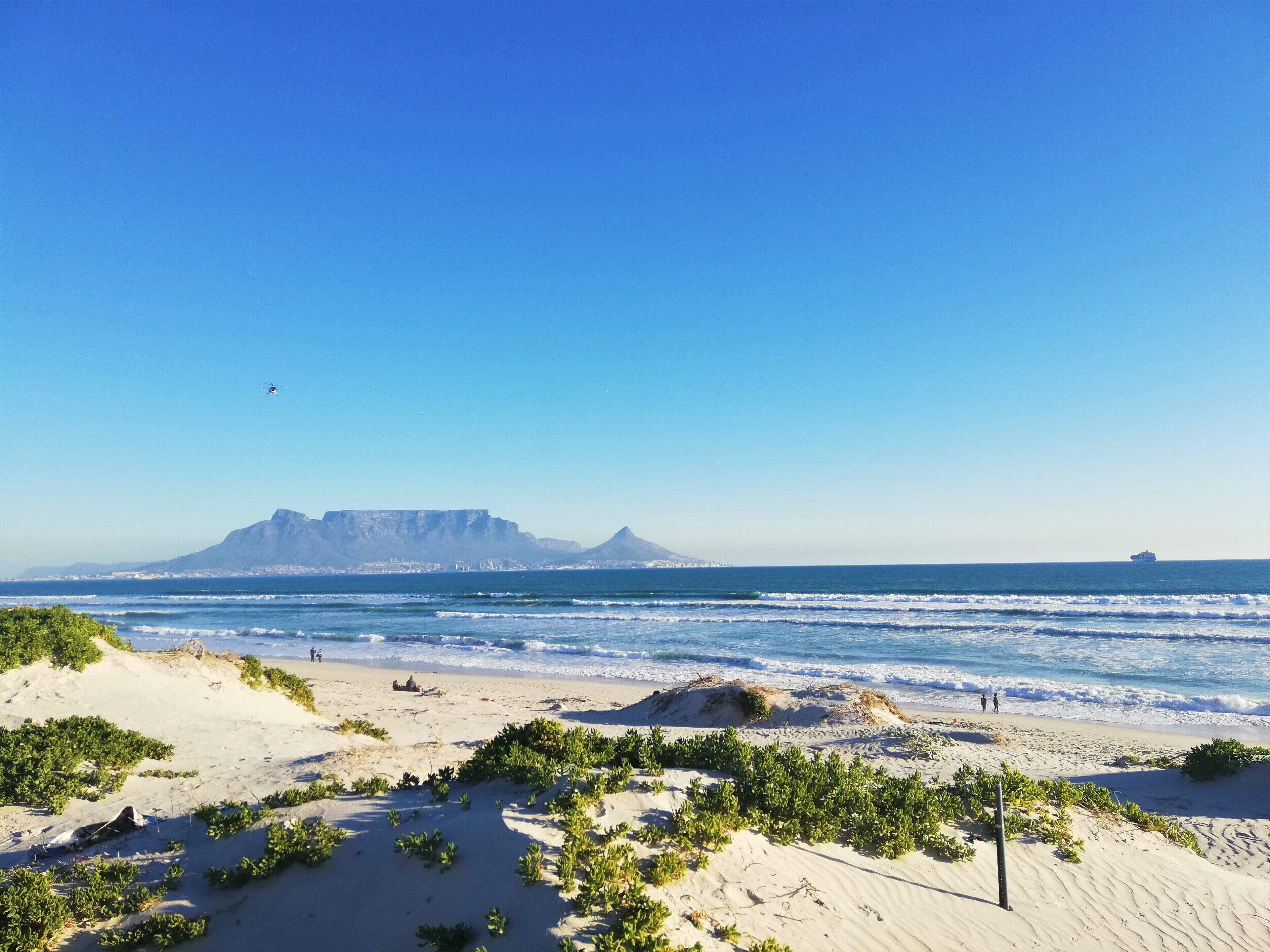 Une plage avec des dunes de sable, un ciel dégagé et une montagne à l’horizon.